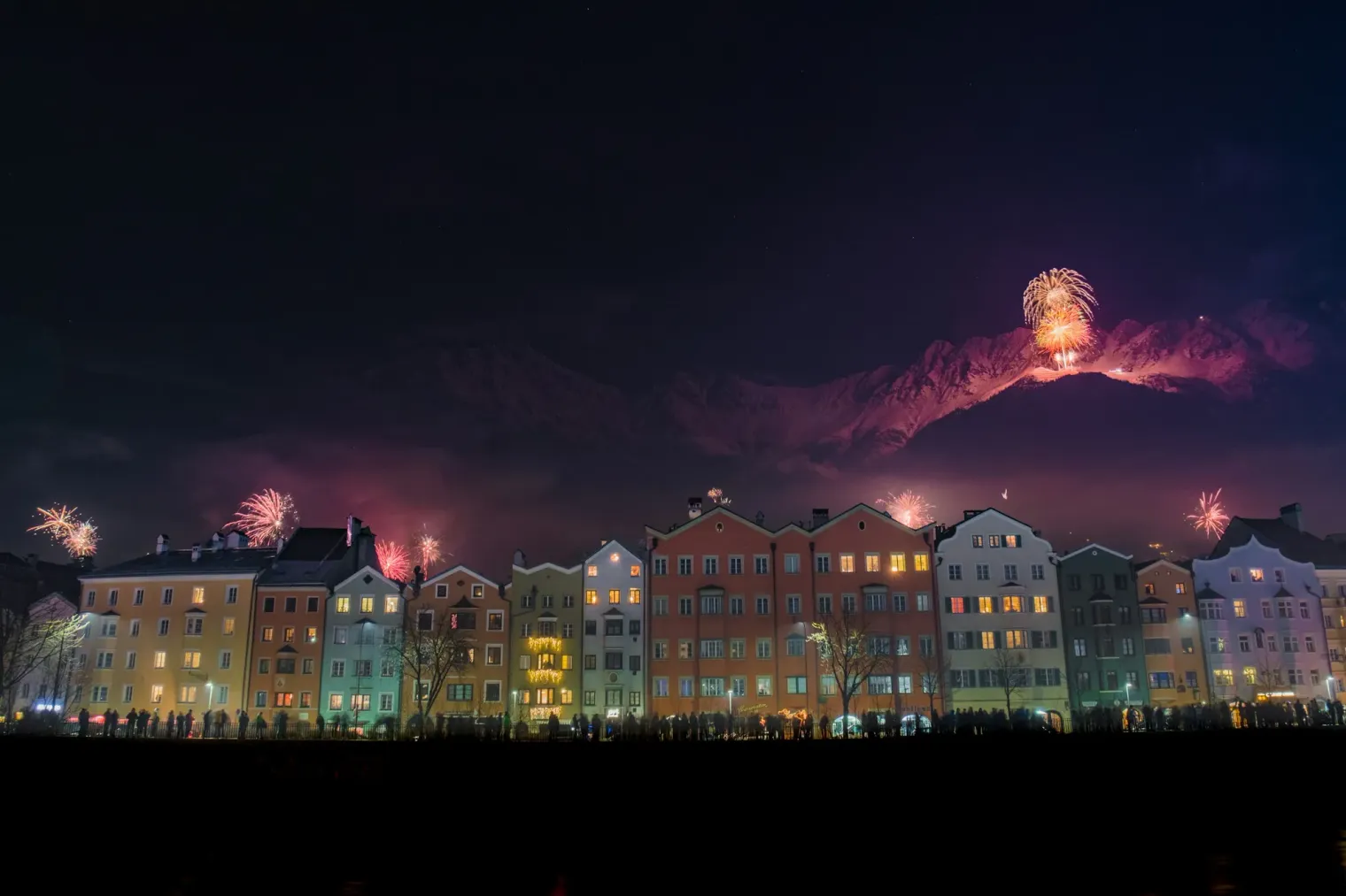 New Year's fireworks over the colourful riverside houses of Innsbruck, Austria, with the snowy Alps behind.